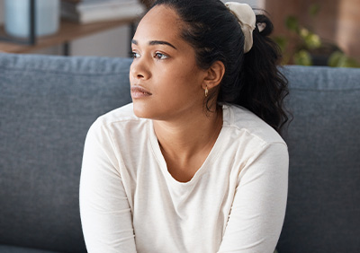 Young woman sitting on a sofa, appearing thoughtful or pensive.