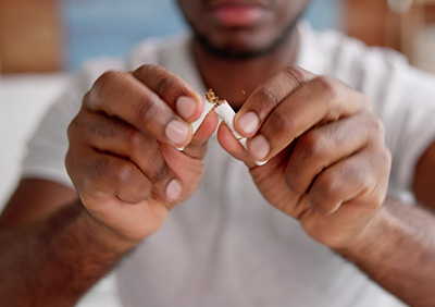 A person breaking a cigarette in half, symbolizing cessation of smoking.