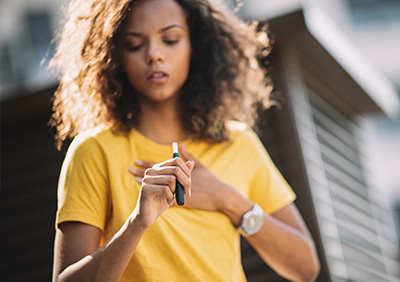 Young woman holding a vape device, looking thoughtful while wearing a yellow shirt.