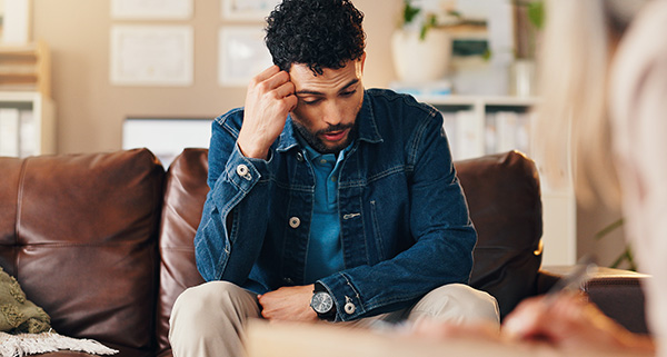 A man sitting in a therapy room, looking contemplative while writing notes.