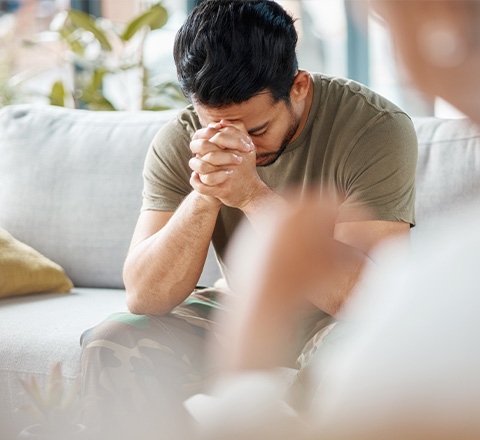 A person sitting on a couch, looking stressed and deep in thought during a therapy session.