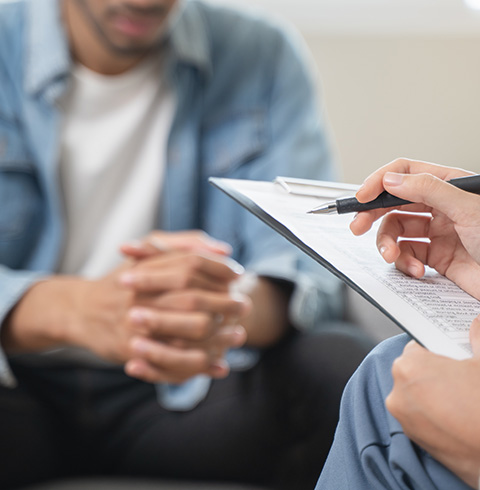 A therapist holding a clipboard while a client listens attentively in a therapy session.