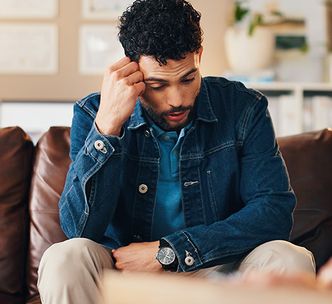 A man appears deep in thought while sitting on a couch in a therapy room.