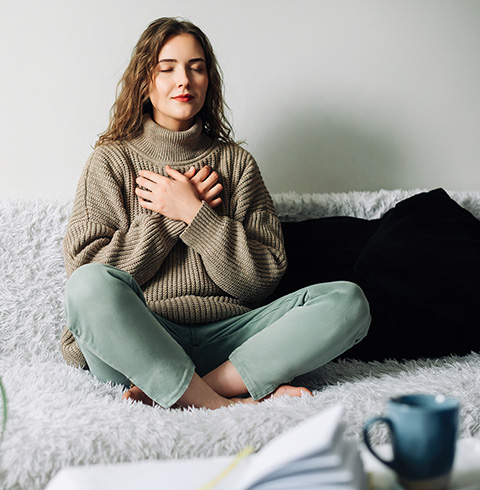 Woman sitting on a couch with hands on her chest, practicing relaxation techniques.