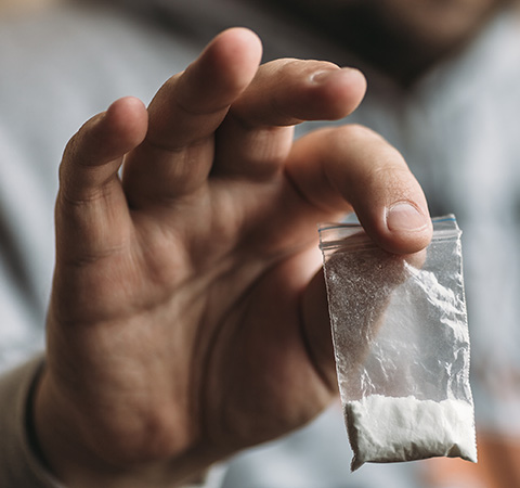 Hand holding a small plastic bag containing a white powder substance, suggesting issues related to substance abuse.