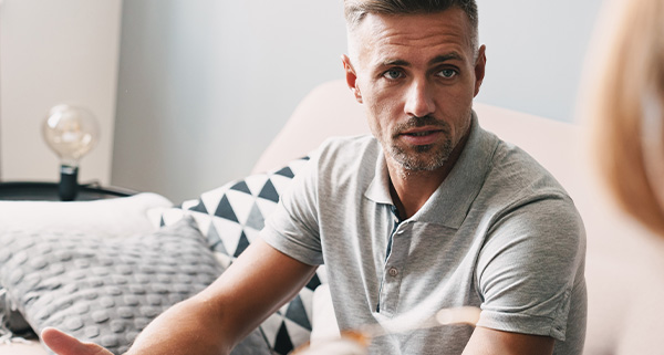A man in a casual shirt discussing something while sitting on a sofa in a therapy room.