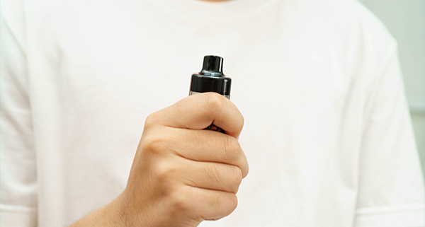 Person holding a black vape device in a casual setting.