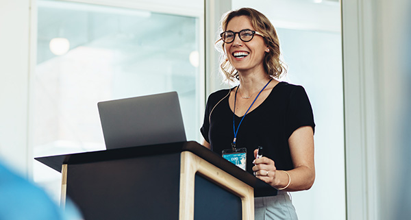 Smiling therapist speaking at a podium, promoting solution focused hypnotherapy.