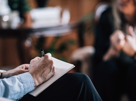 person undergoing therapy while a man writes in a notepad